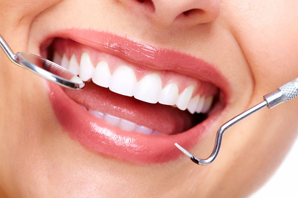 A closeup view of a beautifully white smile with a dental mirror and other tool held nearby.