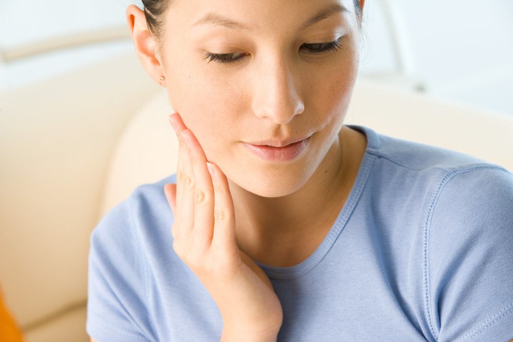 A beautiful, young woman with her hair held back holds her jaw in discomfort.