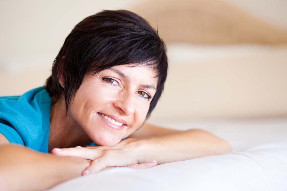 A pretty woman with a short, brunette haircut lying down with her face resting on her hands.